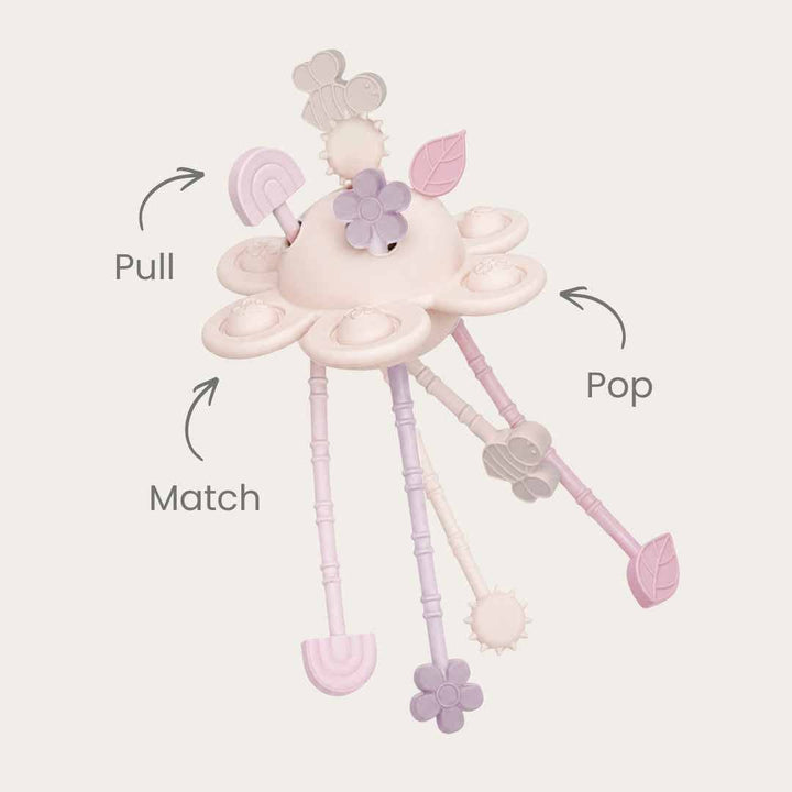 A pastel baby sensory toy with dangling tabs and printed callout arrows and labels reading &