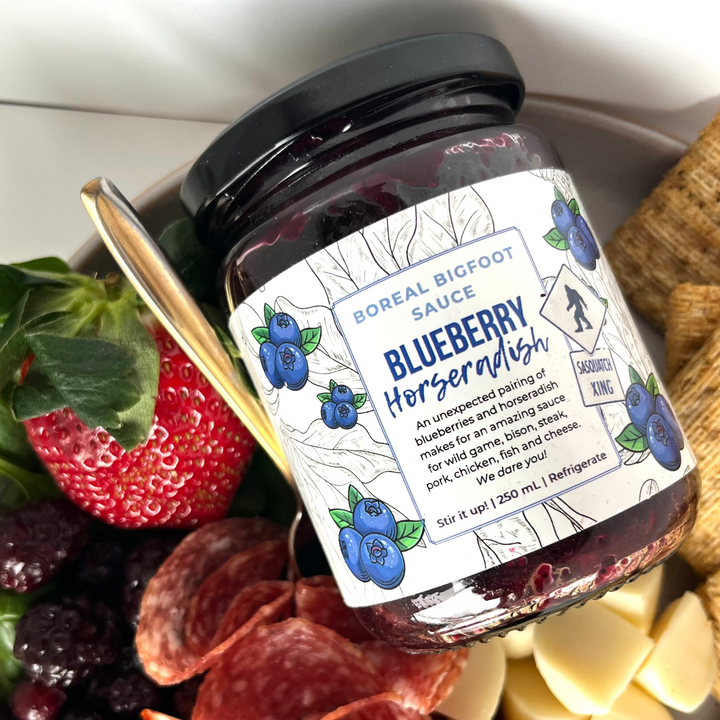 Jar of Blueberry Horseradish sauce on a charcuterie board with fruits and cheese.