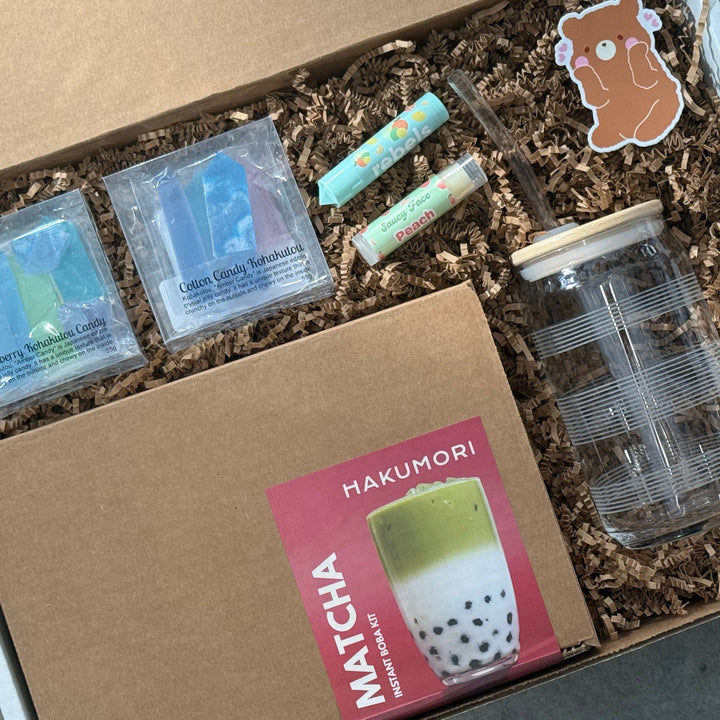 Box containing matcha-themed items including a glass jar, packets, and a card with 'Hakumori' branding.