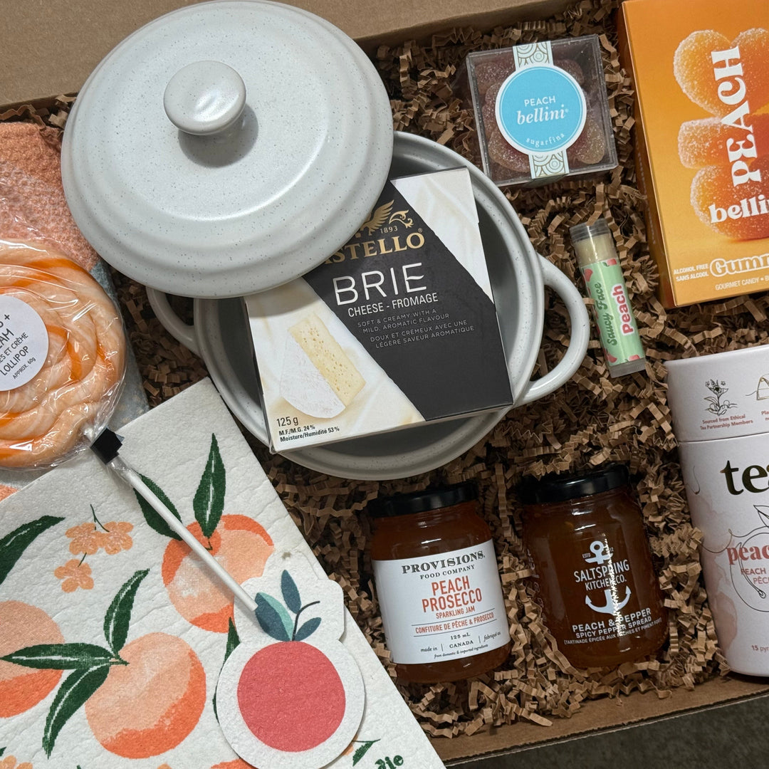 Gift box with assorted items including a jar of brie, peach bellini gummies, and tea.