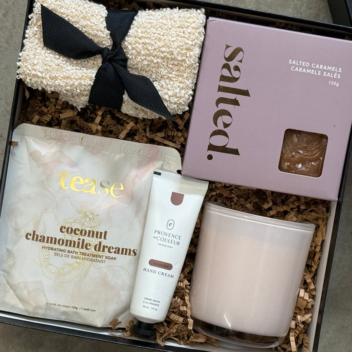 Gift box with products including a candle, cream, and bath bomb on a gray surface.