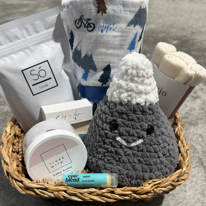 Basket with various items including a crocheted mountain, soap, and other products on a concrete surface.