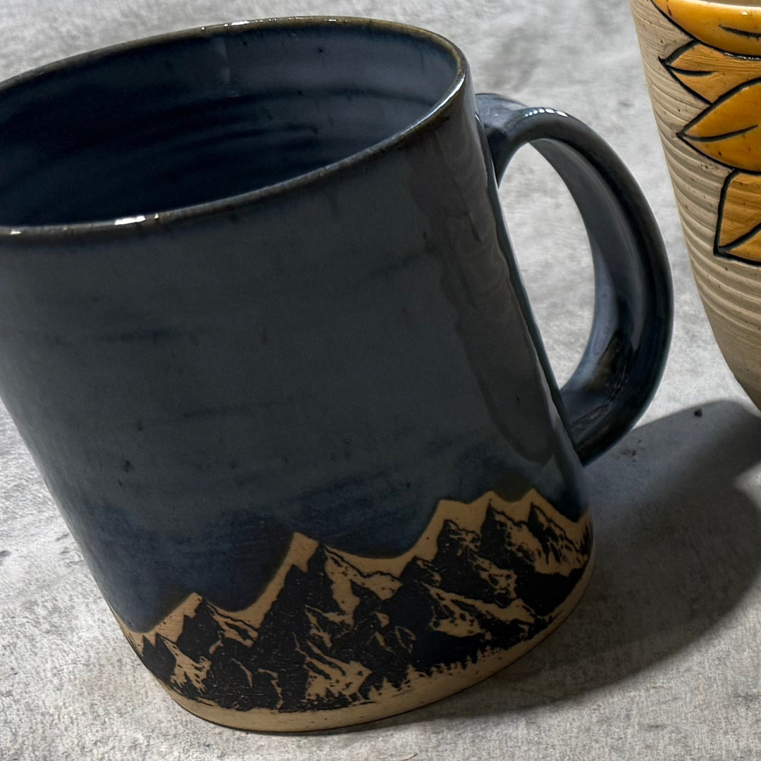 Four ceramic items including a mug, two mugs with floral patterns, and a decorative bowl on a gray surface.