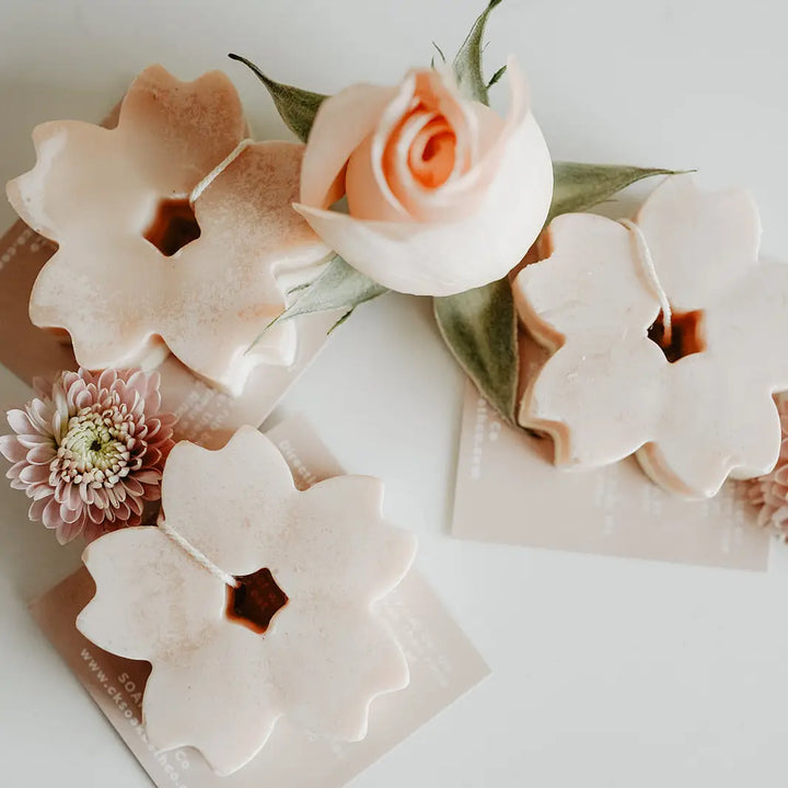 Handcrafted flower-shaped soap bars with a pomegranate scent, displayed with artificial flowers and greenery in the background.
