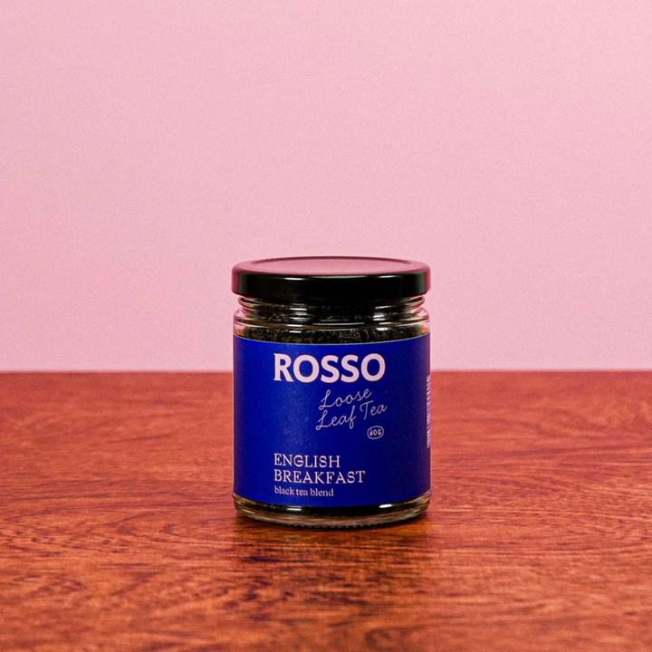 Jar of Rosso English Breakfast tea on a wooden surface with a pink background