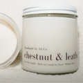 Candle with a visible wick and a white container labeled 'chestnut & leather' on a light background.