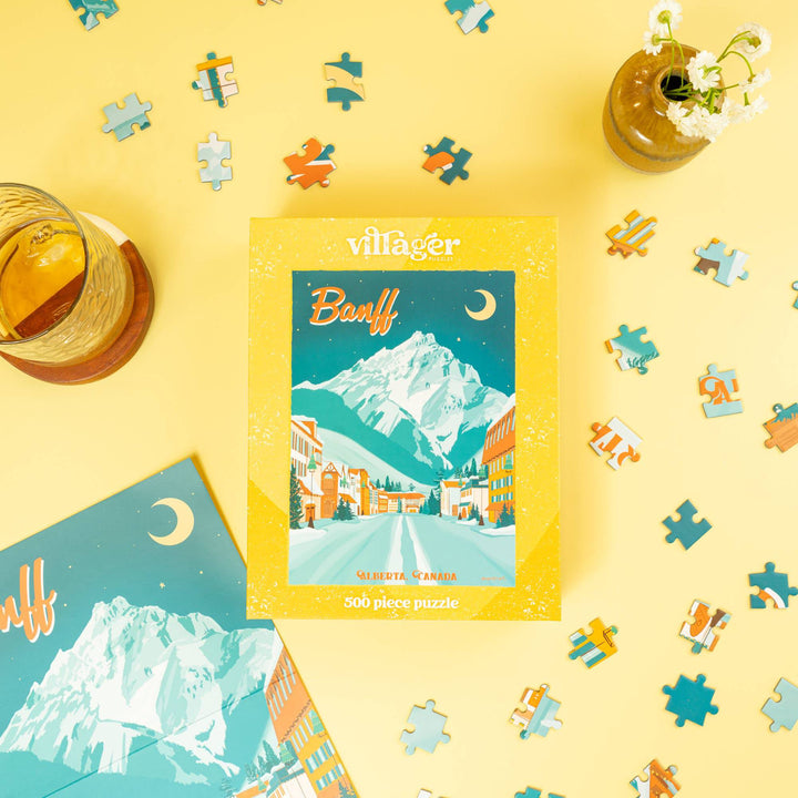 Villager Banff puzzle packaging on a yellow background with puzzle pieces scattered around
