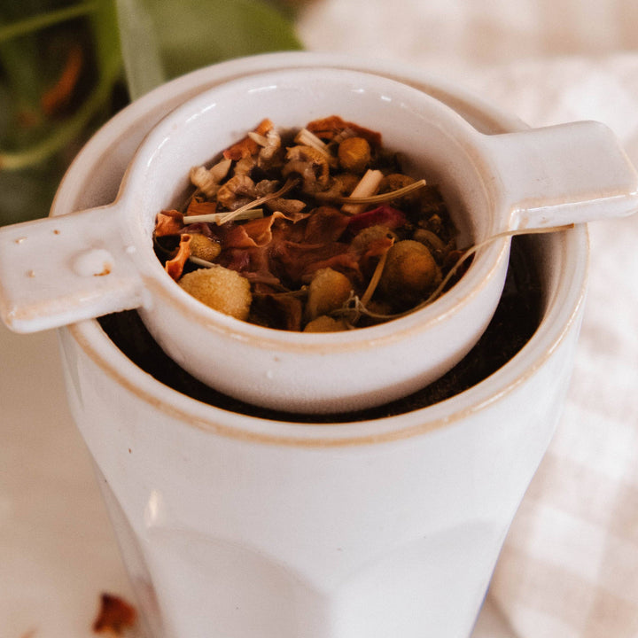 Tea leaves in a white ceramic scoop with a blurred green plant background