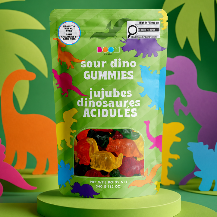 A stand-up pouch of rainbow sour dinosaur gummies displayed on a green pedestal against a colorful background with dinosaur silhouettes and palm leaves. The package is lime green with multicolor dinosaur shapes and text reading &