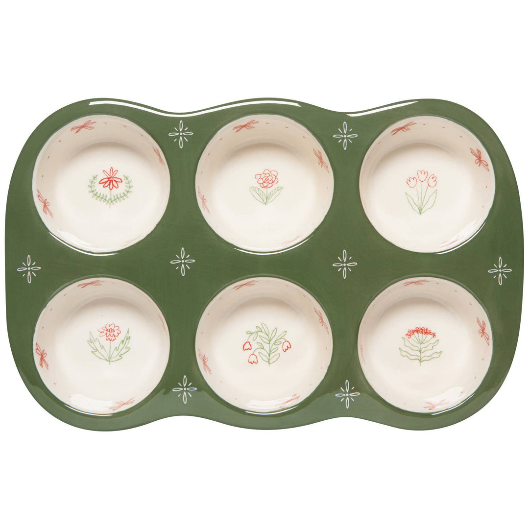A six-cup muffin tin with a dark green exterior and cream-colored interiors decorated with small floral motifs, shown on a plain white background.