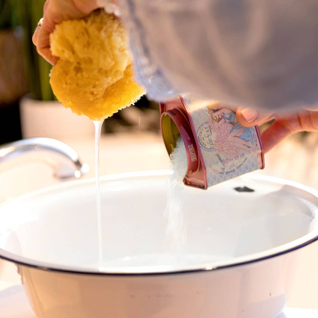 Person pouring milk from a carton into a white container with a yellow sponge.