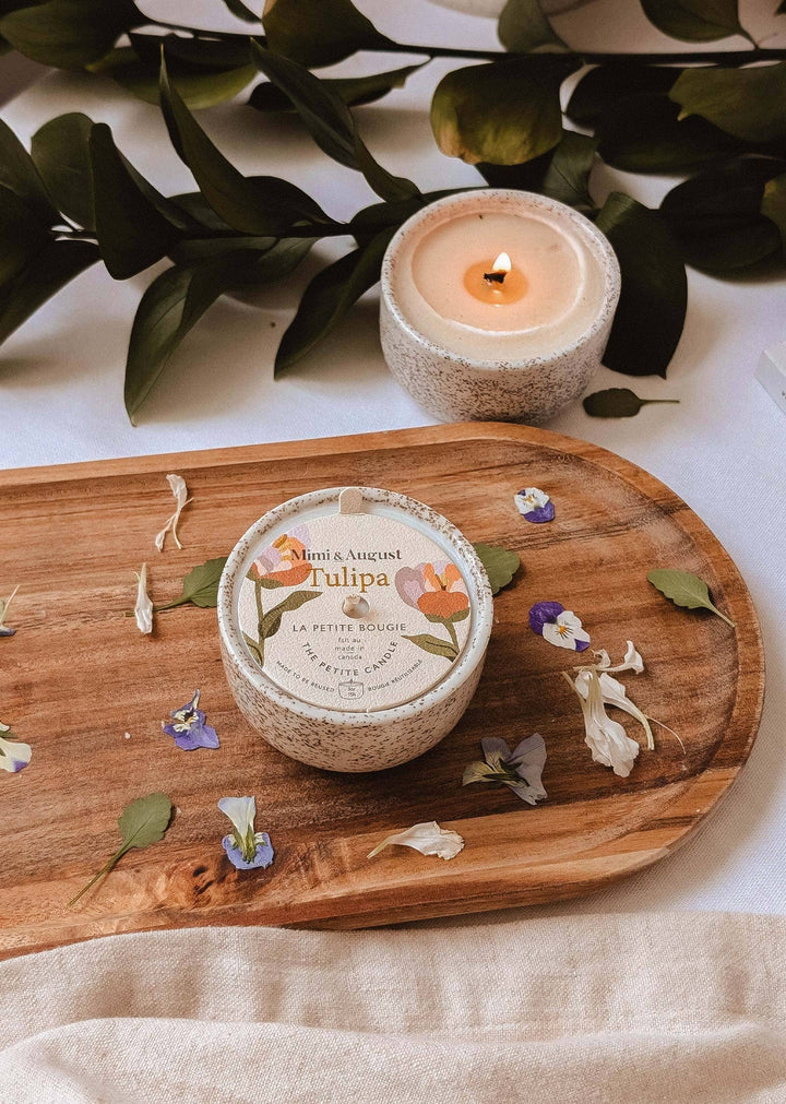 Candle and container on a wooden board with flowers and leaves