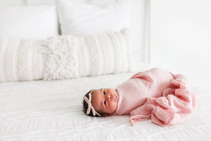 Two Lulujo Baby cotton swaddle blankets, one with strawberry print and one in ballet slipper pink, soft and breathable for babies.