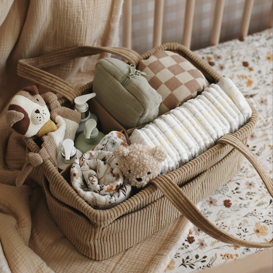 Basket with baby items in a crib with beige bedding and floral sheet