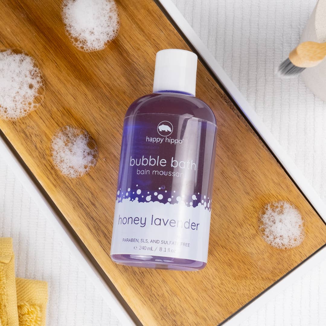 Bottle of happy hippie honey lavender bubble bath on a wooden board with bubbles.