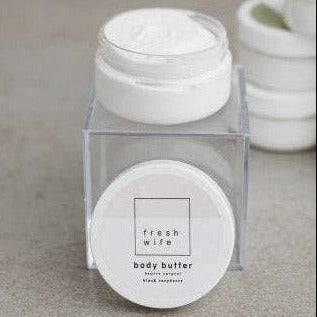 Jar of body butter with a clear lid on a neutral background