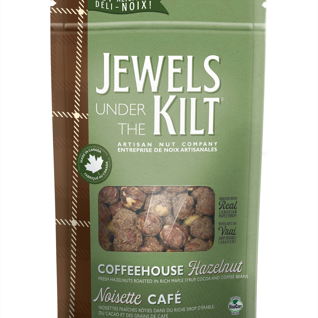 A stand-up pouch of Jewels Under The Kilt Coffeehouse Hazelnut Noisette Café, featuring a sage green background with a brown vertical stripe on the left, a clear window showing the hazelnuts inside, and white text.