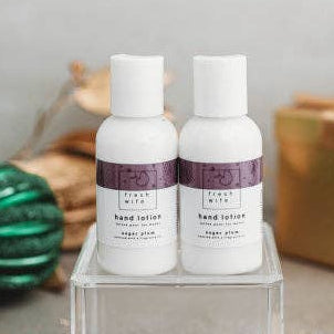Two white bottles of Kith body wash with purple labels, displayed on a clear acrylic block with Christmas ornaments and wrapped gifts in the background.