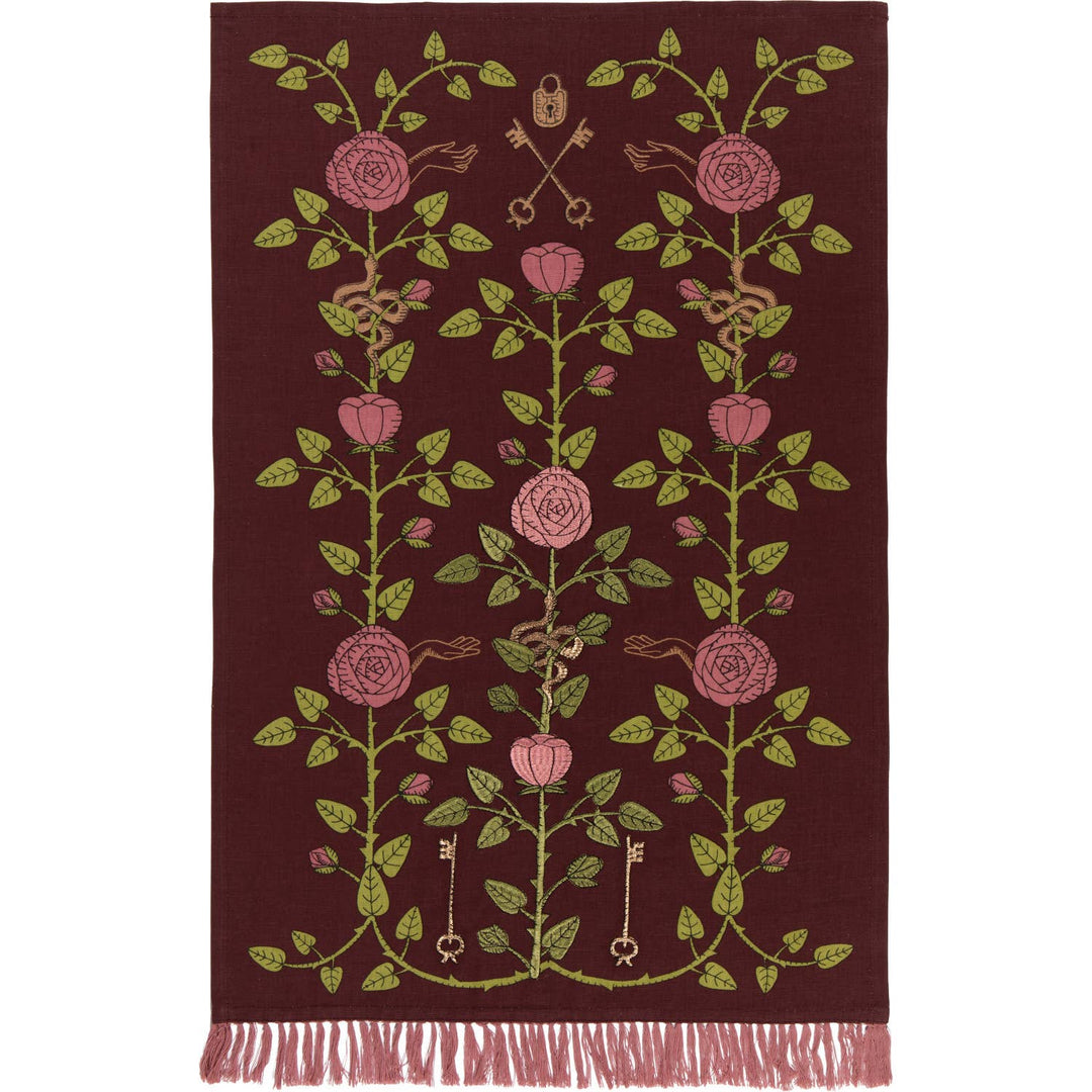 A rectangular burgundy rug with a vertical floral pattern in pink and olive green, featuring decorative keys and a fringed bottom edge.