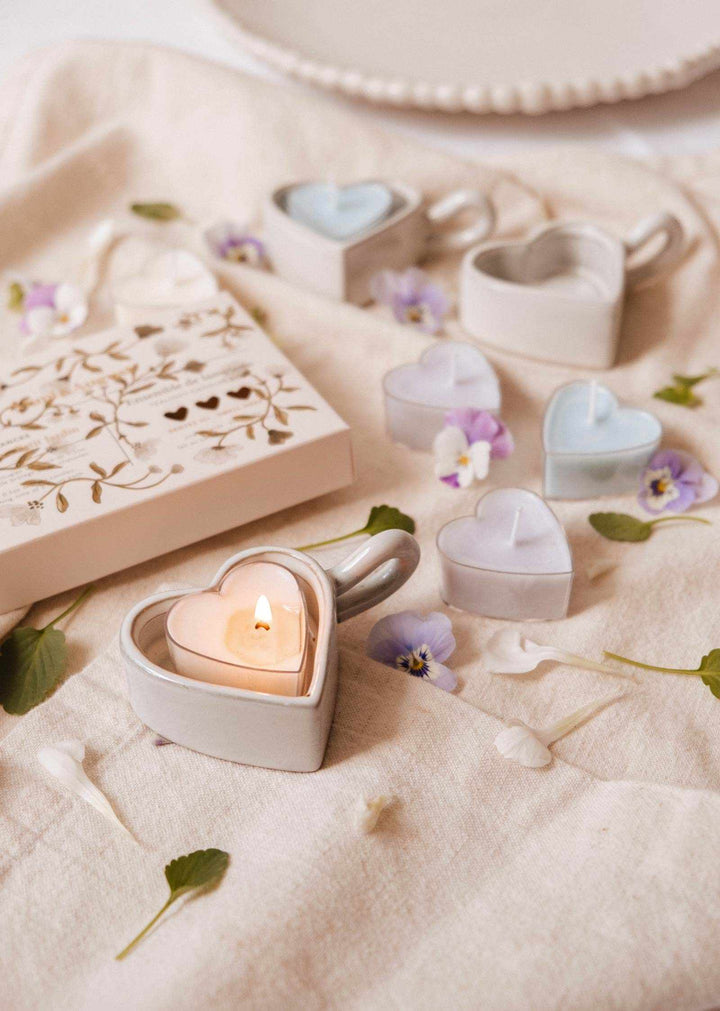 Heart-shaped candles on a soft surface with flowers and a decorative box.