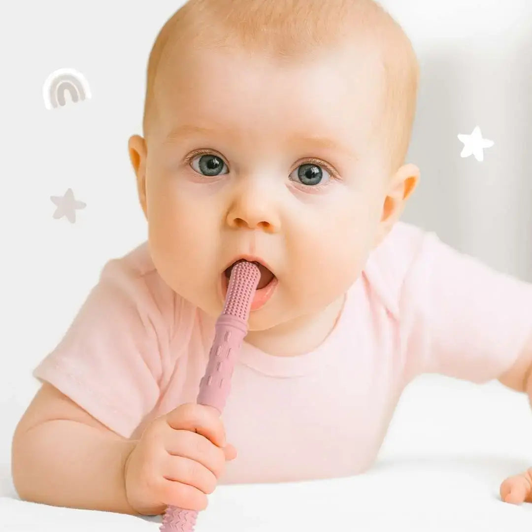 Baby holding a pink baby toothbrush with a plain background