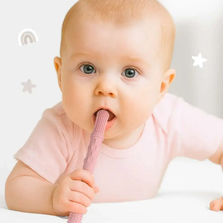Baby holding a pink baby toothbrush with a plain background