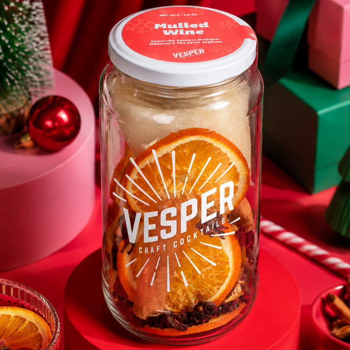 Vesper craft cocktail mix jar with Christmas decorations on a red background