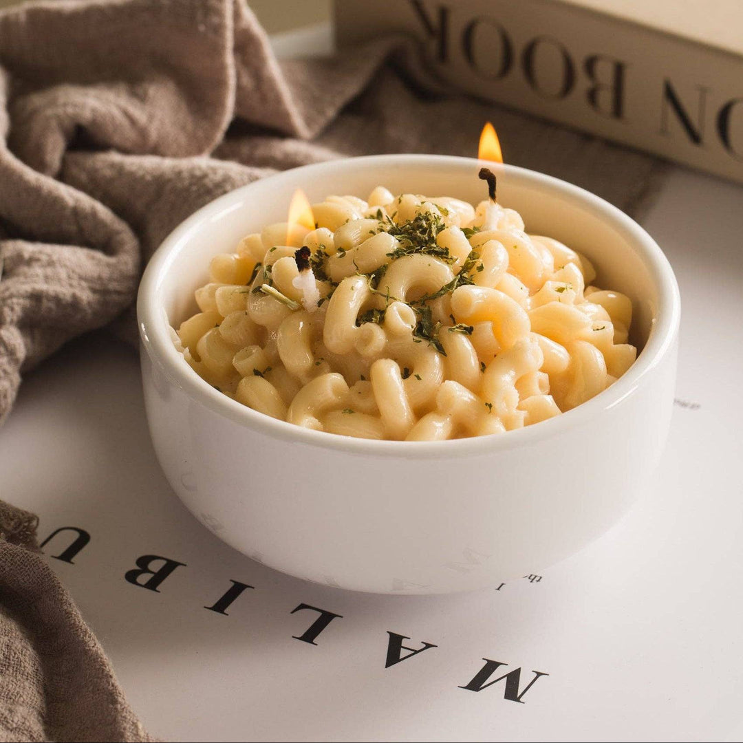 Candle in a bowl of pasta with a book and towel in the background