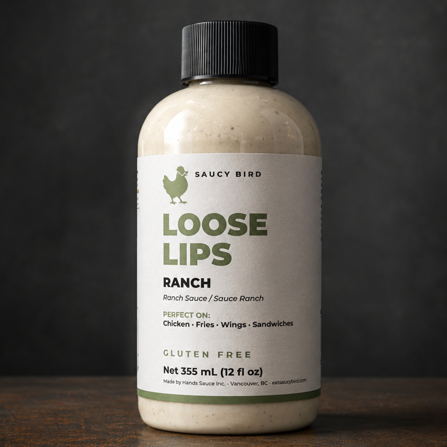 A bottle of Loose Lips Ranch Ranch Dress with a black cap and a white label, set on a dark wooden surface against a dark gray background.
