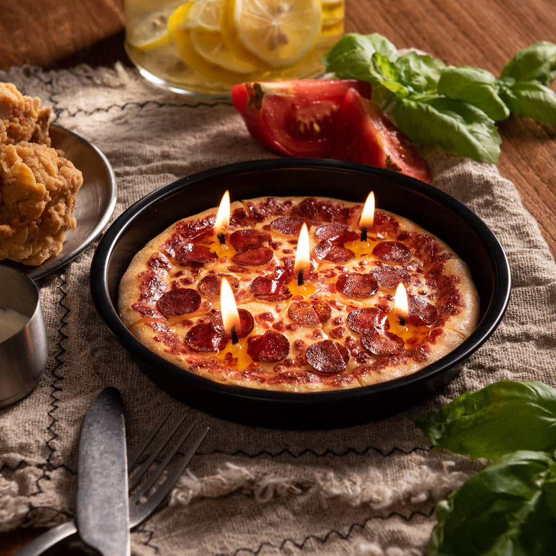 Candle-shaped pizza with lit candles on a wooden table with a glass of lemonade and fried chicken.