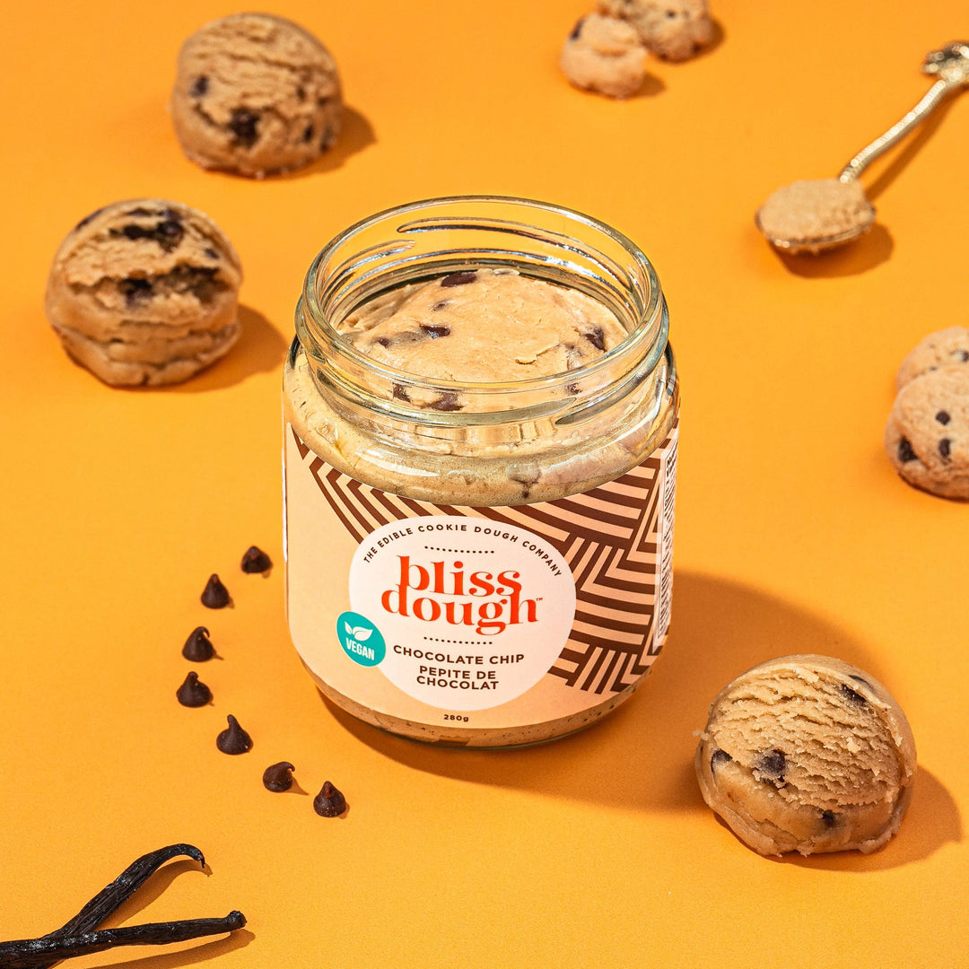 Jar of 'bliss dough' chocolate chip cookie dough on an orange background with cookies and vanilla beans.