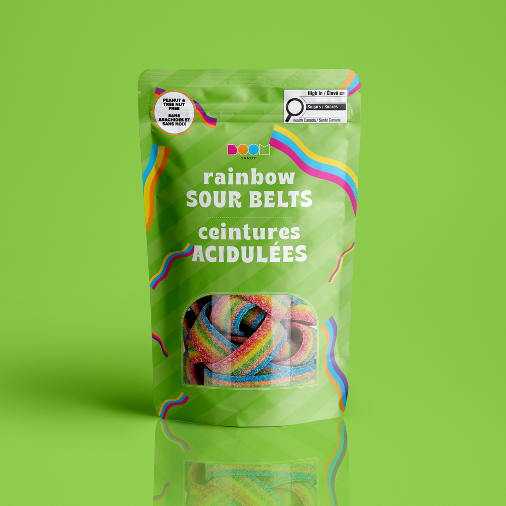 A stand-up pouch of rainbow sour belts candy on a bright green background. The packaging is light green with colorful wavy lines and white text reading 'rainbow SOUR BELTS' and 'ceintures ACIDULÉES'.
