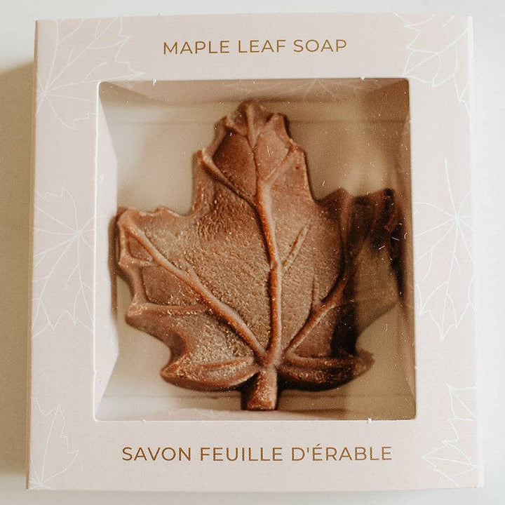 A maple leaf-shaped soap bar displayed inside a square white box with a clear window. The box is labeled &