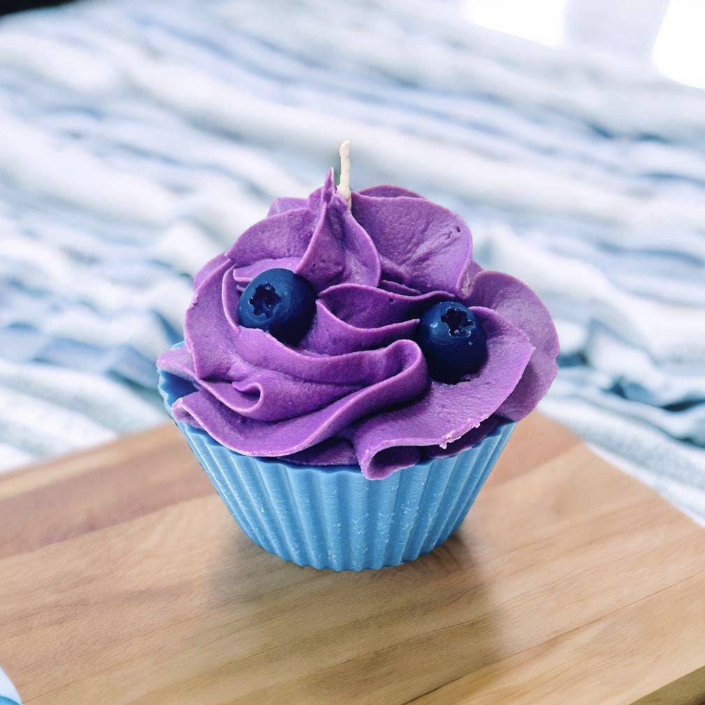 Cupcake with purple frosting and blueberries on a wooden surface with a striped fabric background