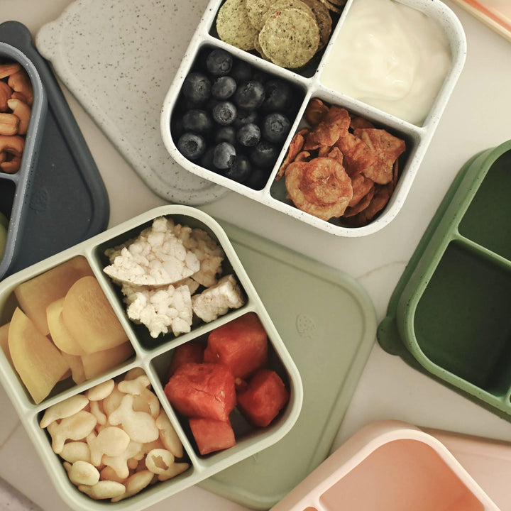 Assorted bento boxes with compartments filled with various foods on a light surface.