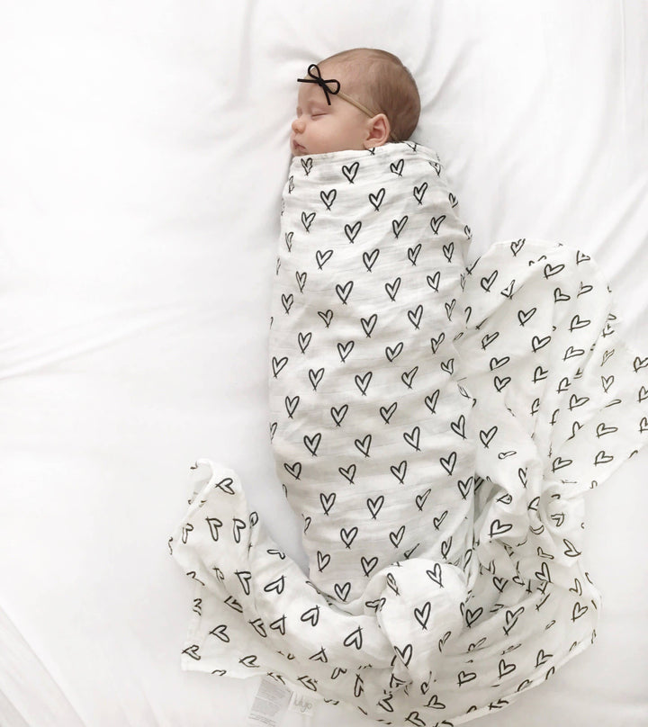 Baby swaddled in a blanket with heart patterns on a white background