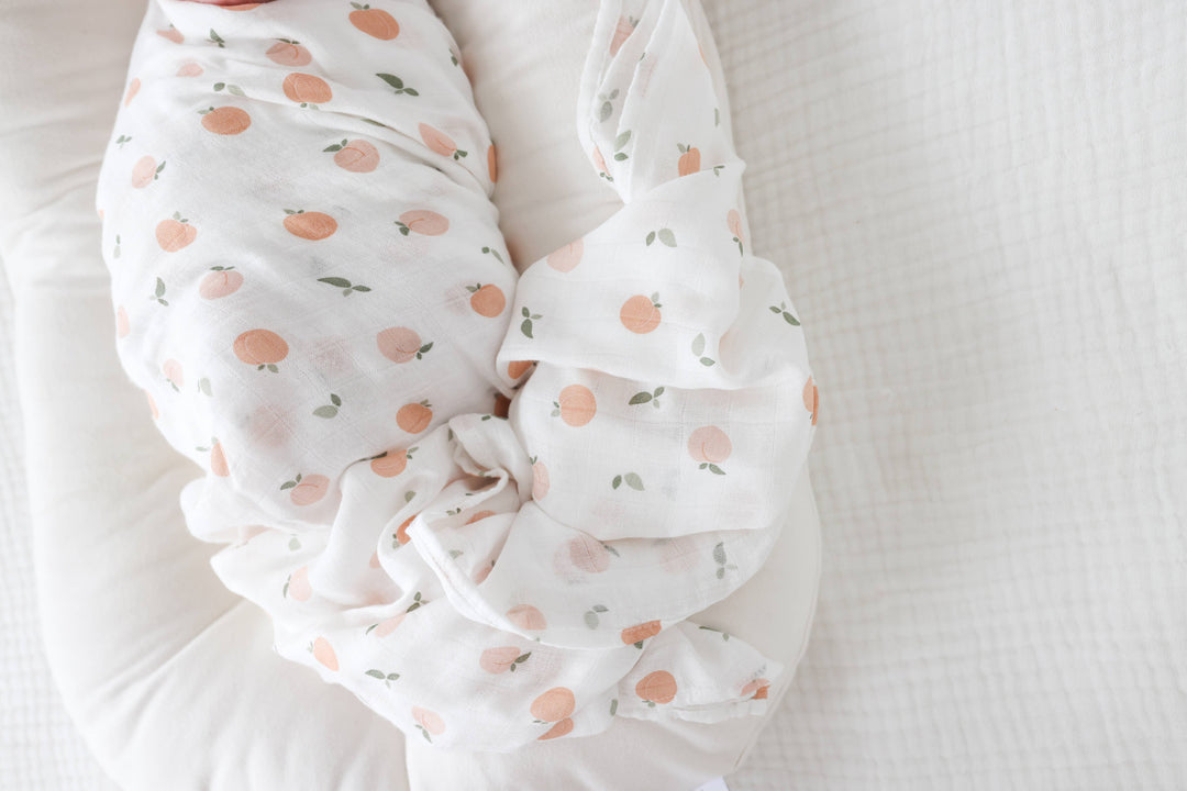 Lulujo Baby muslin cotton swaddle blanket with peach fruit pattern, soft and lightweight for newborns and infants.