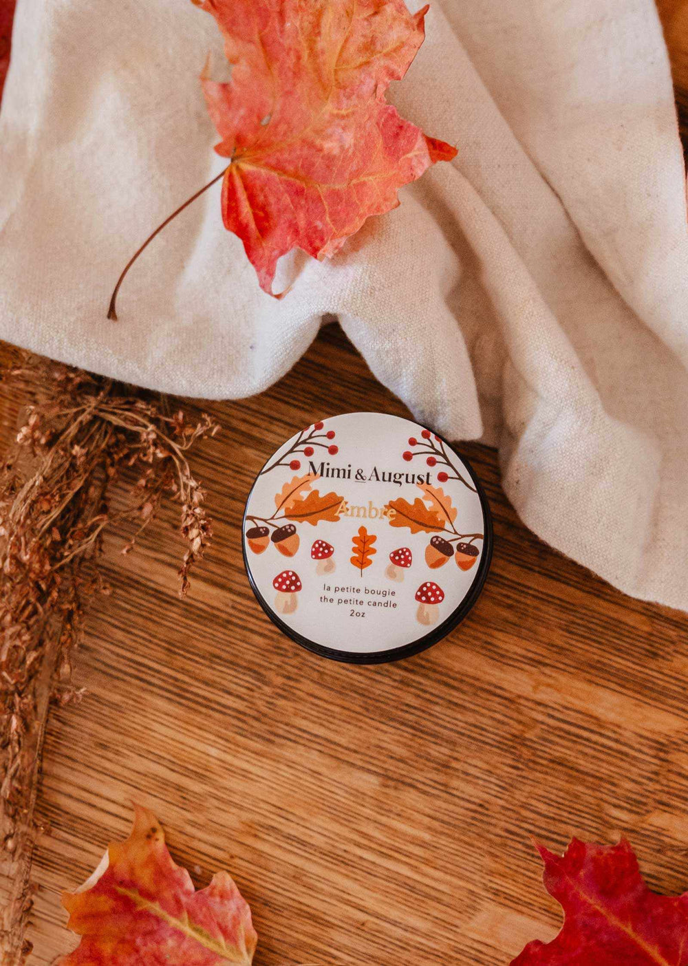 Circular product with 'Mimi & August' branding on a wooden surface with autumn leaves.
