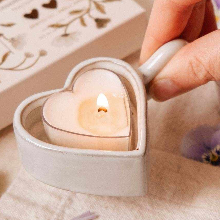 Heart-shaped candle being lit on a soft surface with decorative elements