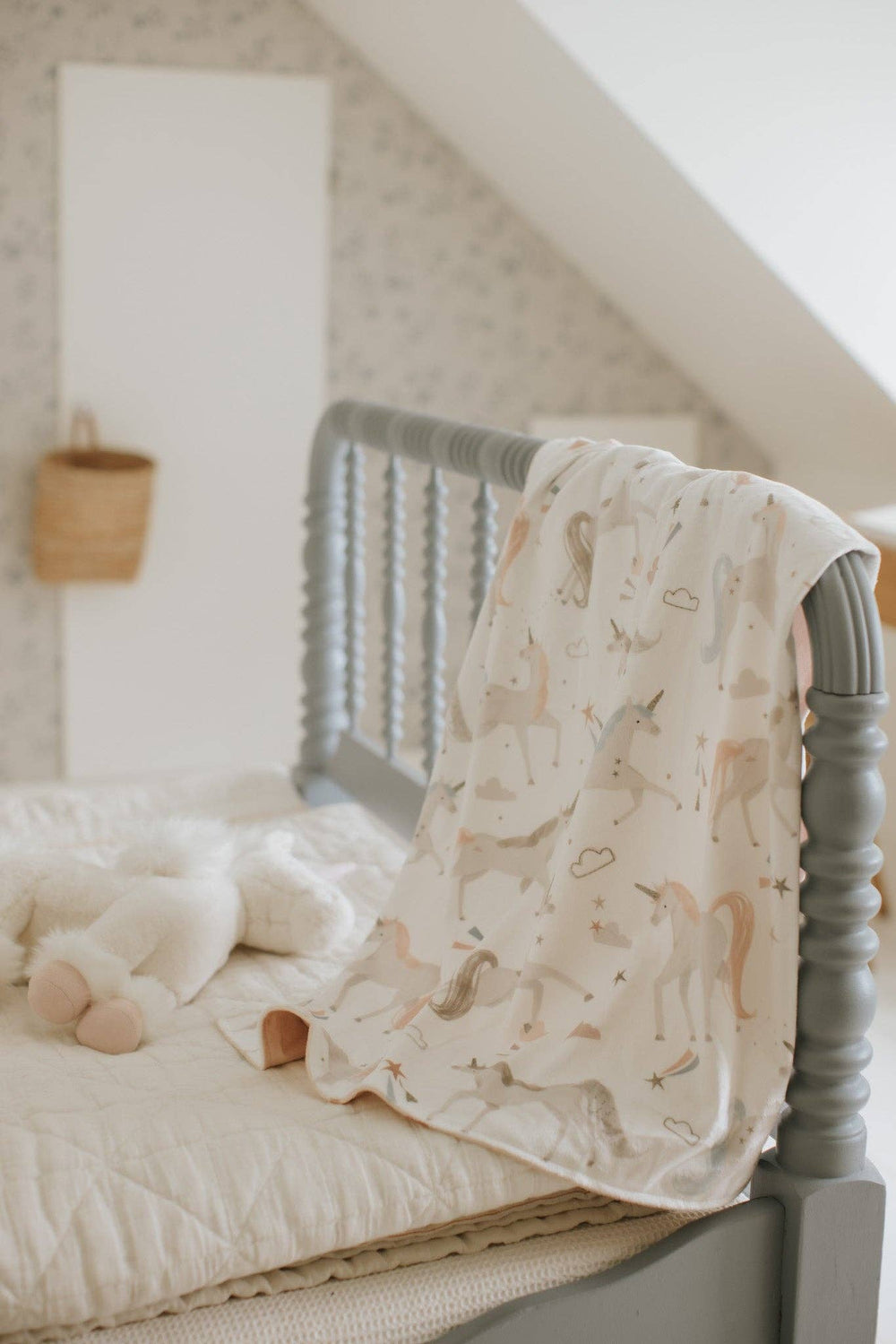 Baby crib with gray metal frame and white bedding, featuring a soft blanket with animal pattern.