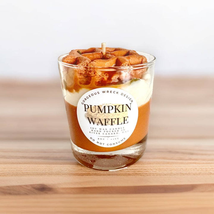 Candle in the shape of a pumpkin waffle with a label on a wooden surface