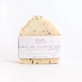 Lemon and rosemary soap bar by Soak Bath Co with fresh lemon slices and rosemary sprigs on a white background.