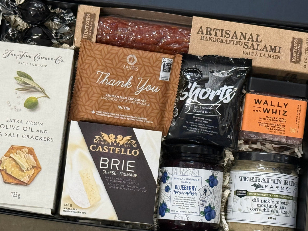 Assorted gourmet food items including cheese, salami, and pickles in a box.