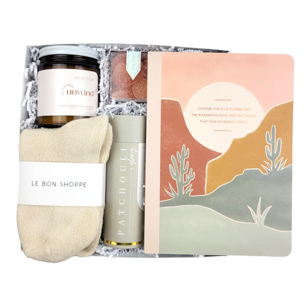 It's time to unwind & relax! We love this collection of luxury self-care items and they will too! Named after the Choose The Wild Places Notebook included for some self-reflection and journaling.   GIFT CONTENTS:  Misiyo Unwind Candle (natural coconut wax naturally scented with lavender, peppermint leaf, & cedarwood) Patchouli Ylang Shower Steamers Le Bonne Shoppe Cloud Socks Sugarfina Tequila Sours Choose The Wild Places Notebook
